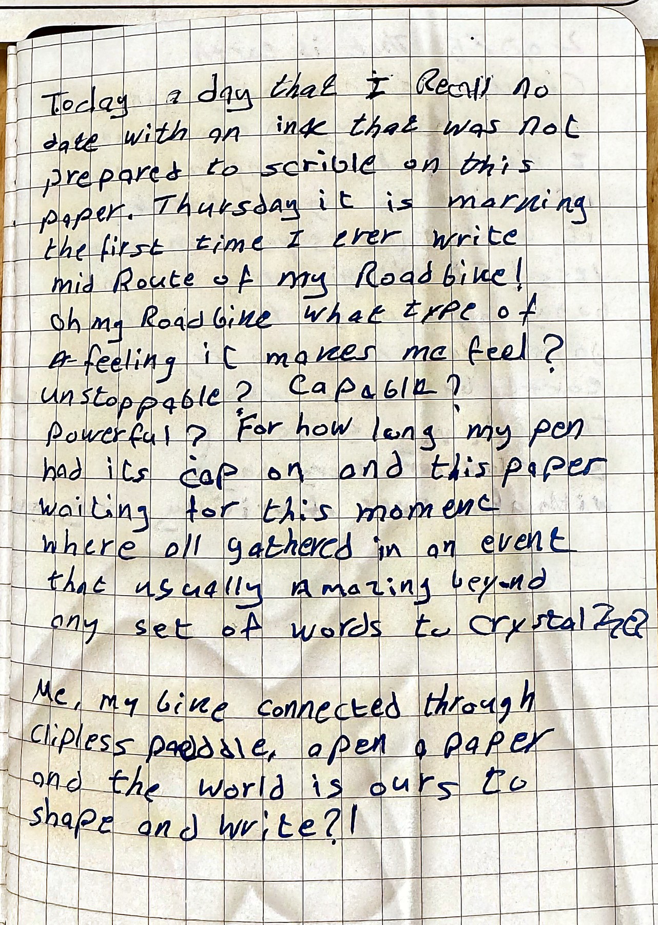 A squared notebook page filled with blue handwriting, photographed on a bench mid-ride